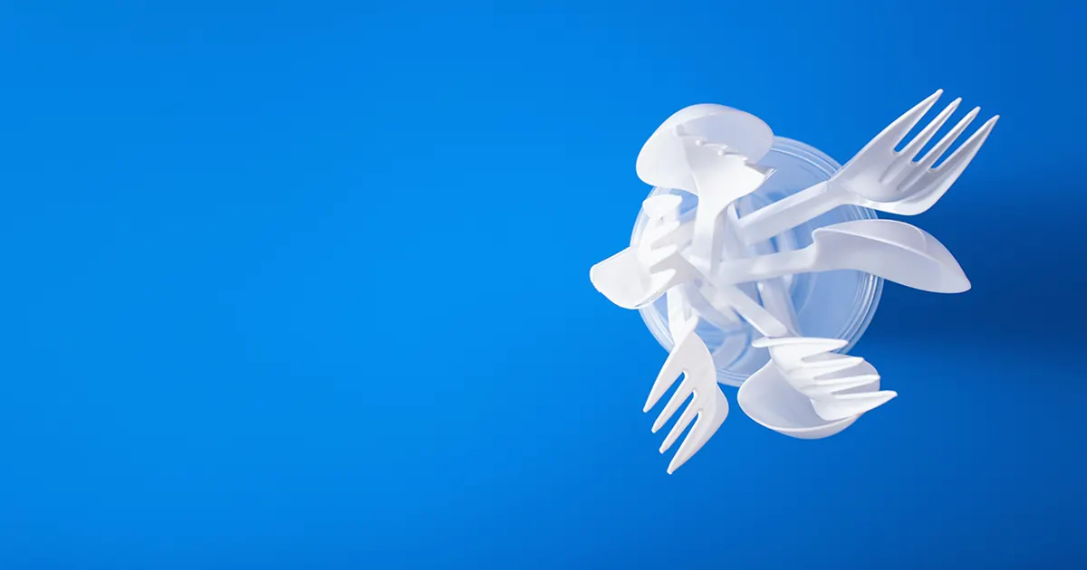 White plastic cutlery in a plastic cup on a sky blue background